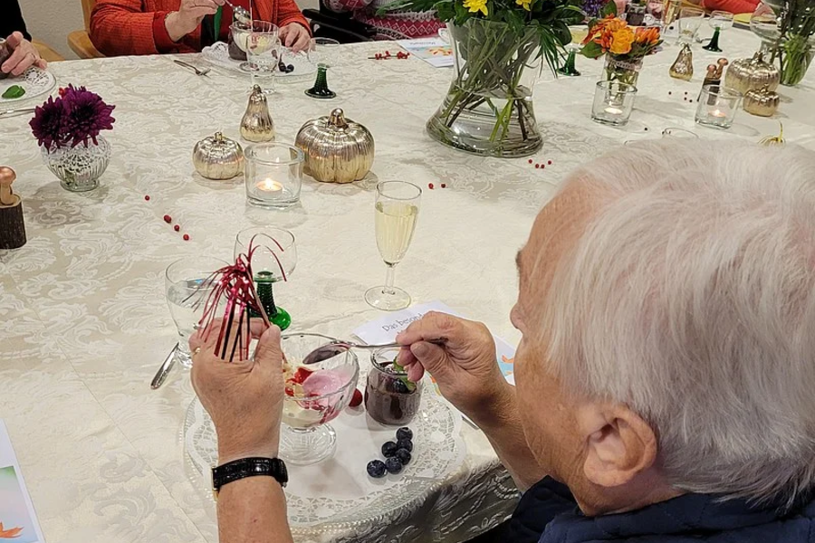 Ältere Frau sitzt an einem gedeckten Tisch und hält einen kleinen Korb mit roten Beeren in der Hand