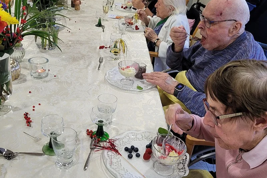 Mehrere ältere Menschen sitzen an einem langen Tisch mit gedeckter Tafel und essen gemeinsam