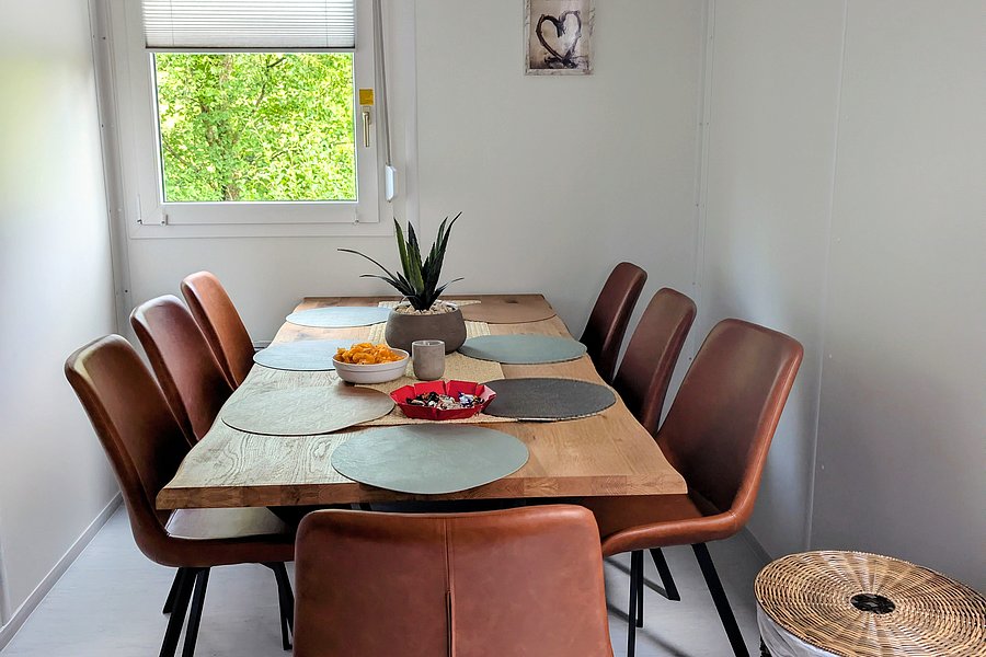 Esszimmer mit rechteckigem Holztisch, sechs braunen Stühlen und einem Wäschekorb aus geflochtenem Material in der Ecke
