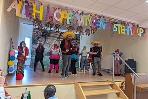 Bunte Karnevalsaufführung mit Tänzern in Kostümen und großen Hüten auf einer Bühne.