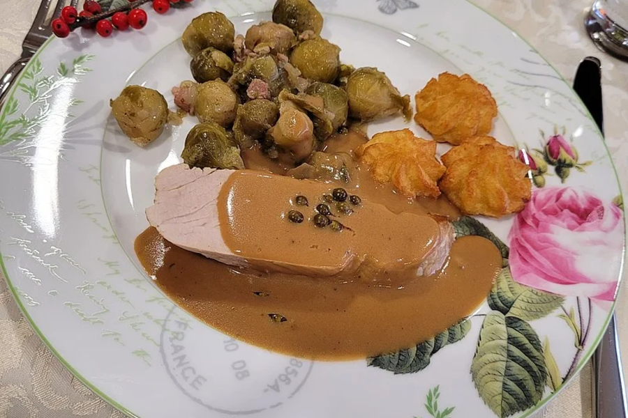 Teller mit einer Scheibe Fleisch in brauner Sauce, Rosenkohl und drei Kartoffelklößen, dekoriert mit roten Beeren und Blumenmuster