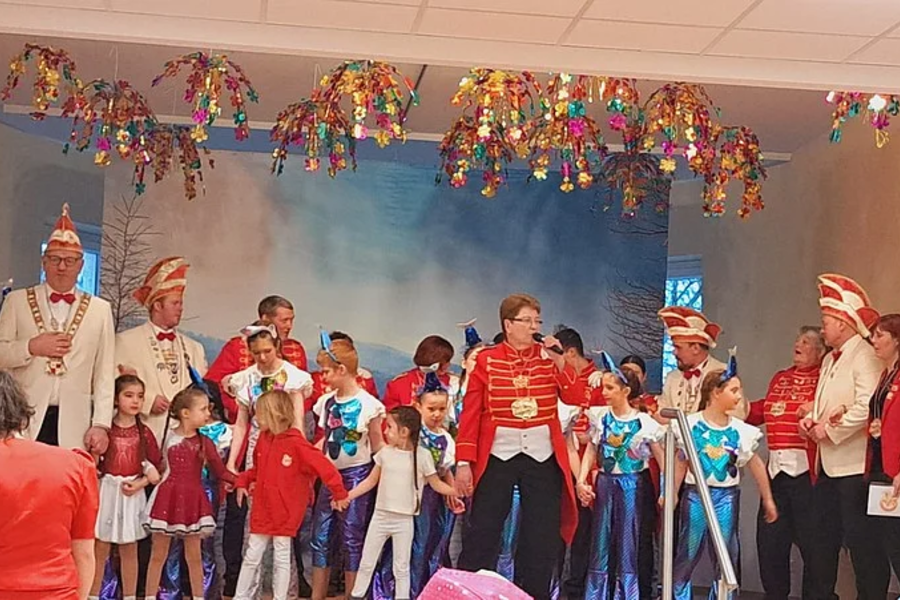 Gruppe von Kindern und Erwachsenen in bunten Kostümen auf einer Bühne mit Girlanden an der Decke