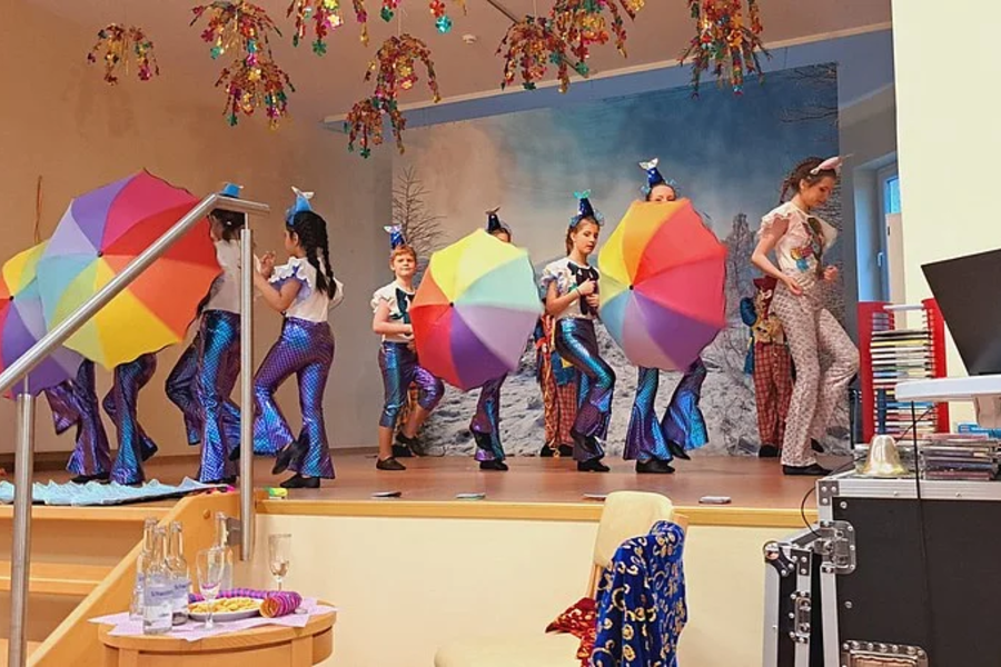 Gruppe von Kindern auf einer Bühne mit bunten Regenschirmen in einer Tanzpose