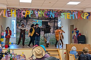 Szenen von einer bunten Aufführung mit Tänzern und Clowns auf einer Bühne, fröhliche Atmosphäre.